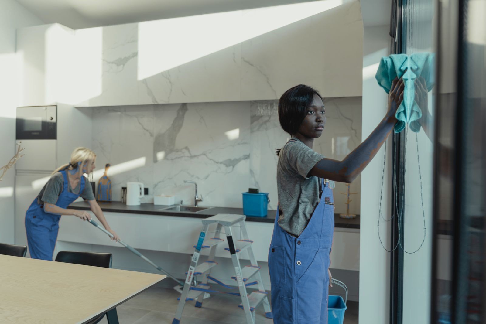 Cleaners wiping a window and mopping floors in a modern home